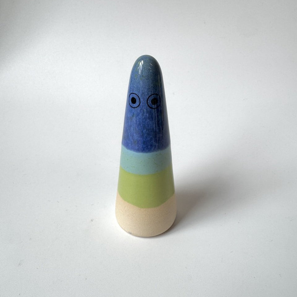 Wilfred Studio Arhoj ghost, featuring a blue top section with painted eyes, a light blue band, a pale green band, and a natural beige base, set against a plain white background.