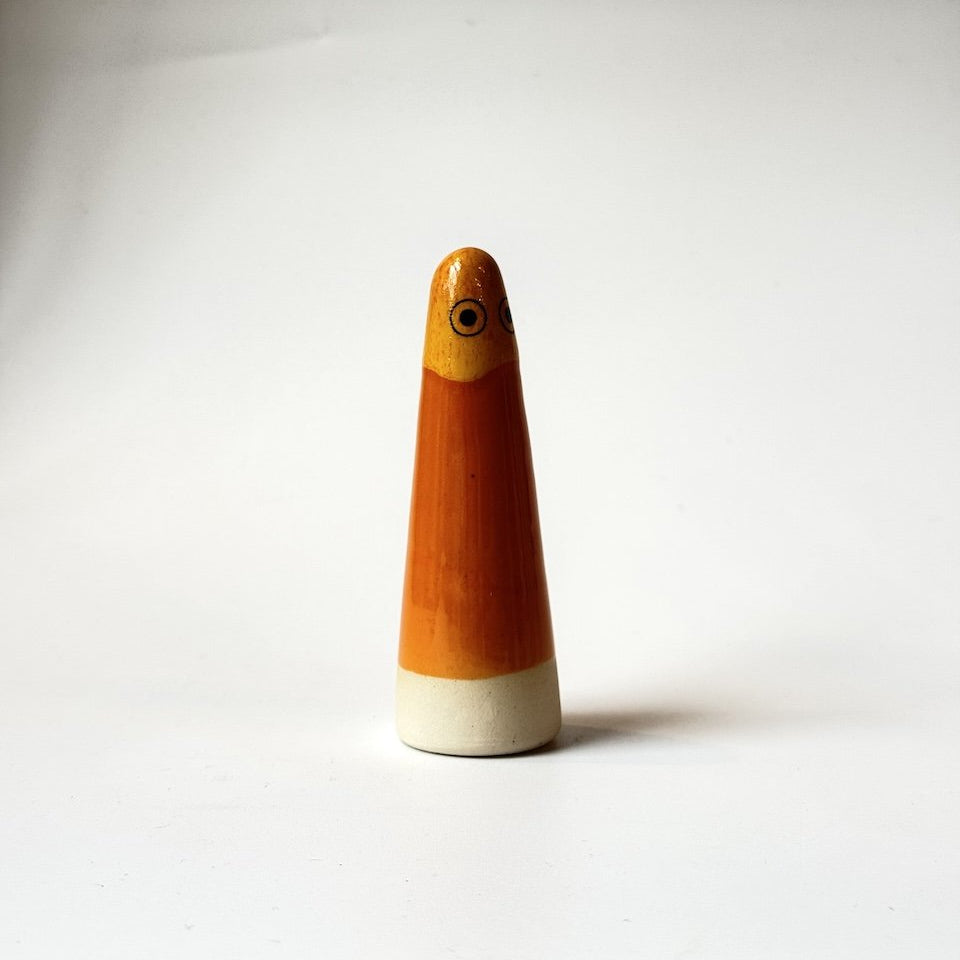 John Studio Arhoj ghost glazed orange and yellow and black-and-white eyes, and it rests on a white base.