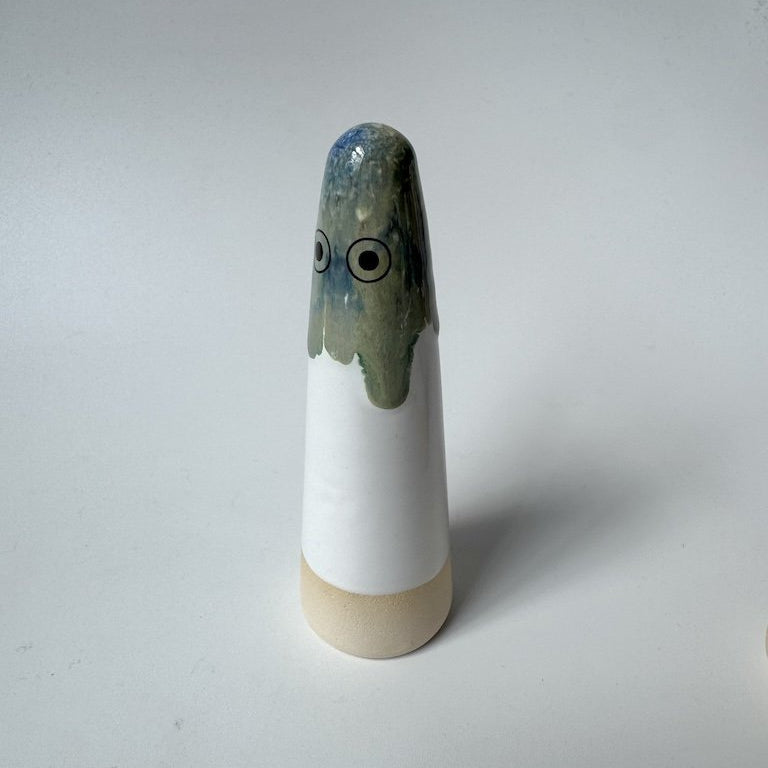 Dahlia Studi Arhoj ghost, with a glossy blue-grey top, large black and white eyes, a white body, and a beige base, photographed on a plain light grey background.