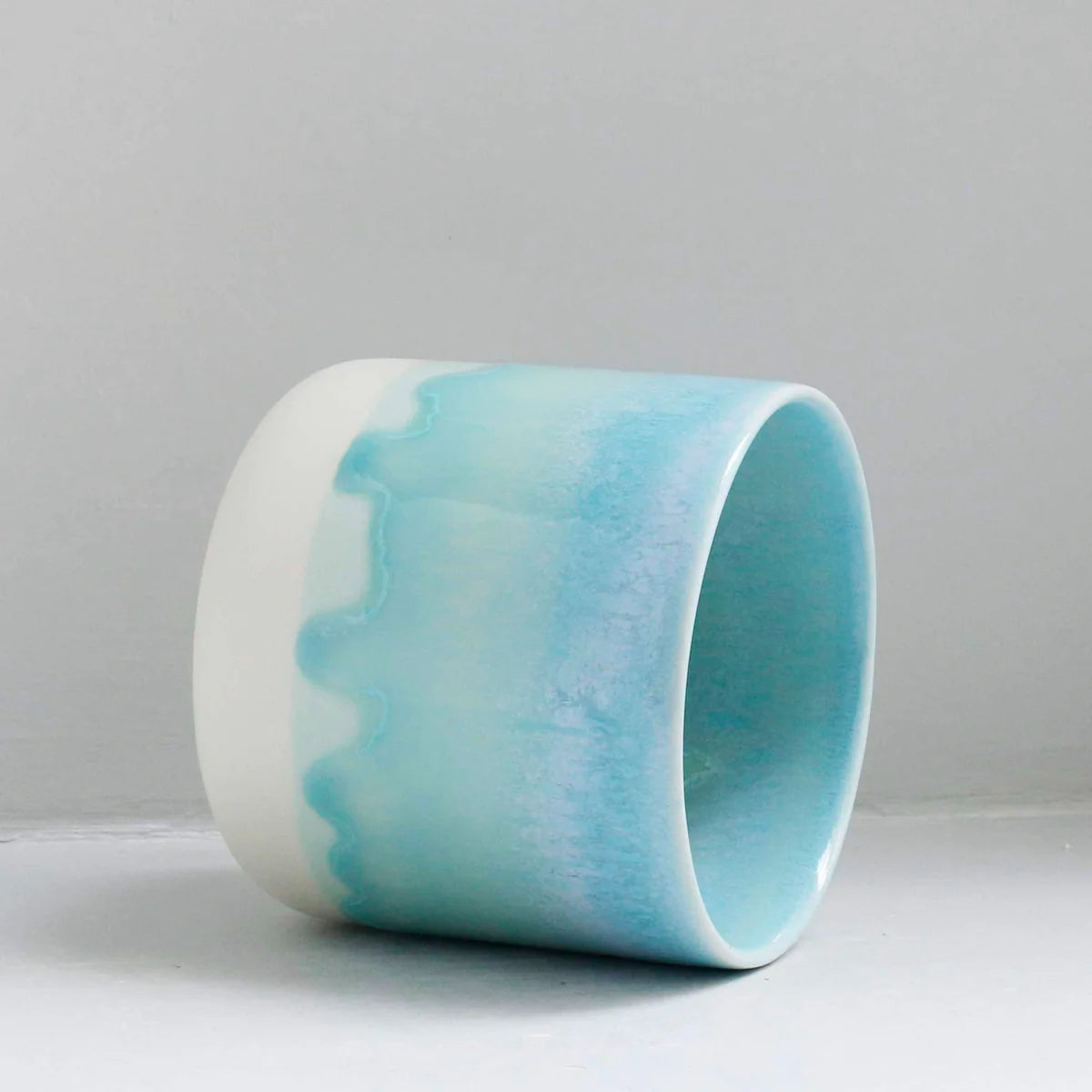 Close up of a white, blue and aqua green handleless cup on its side