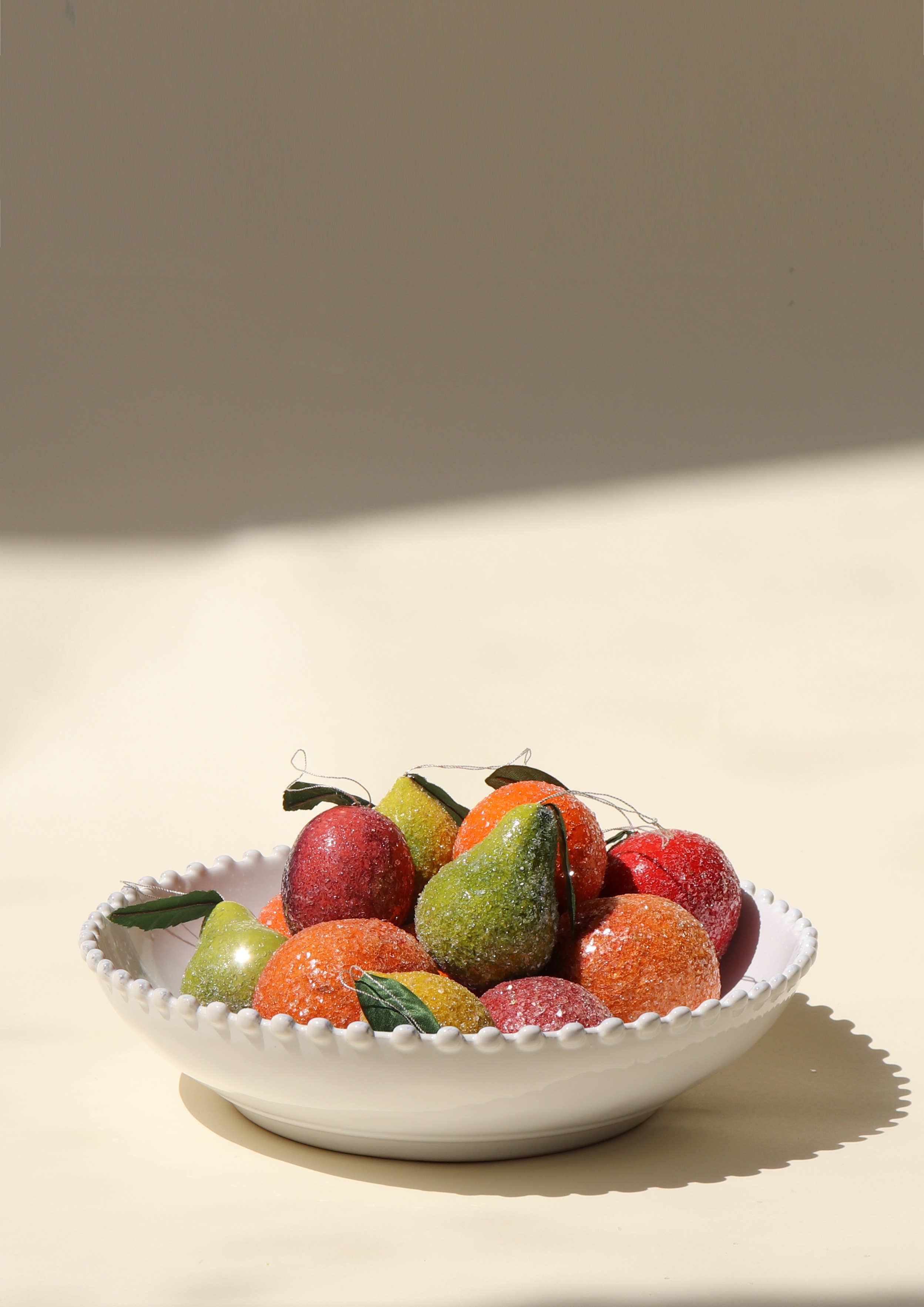 Decorative bowl with colorful sparkly fruit ornaments on a neutral background