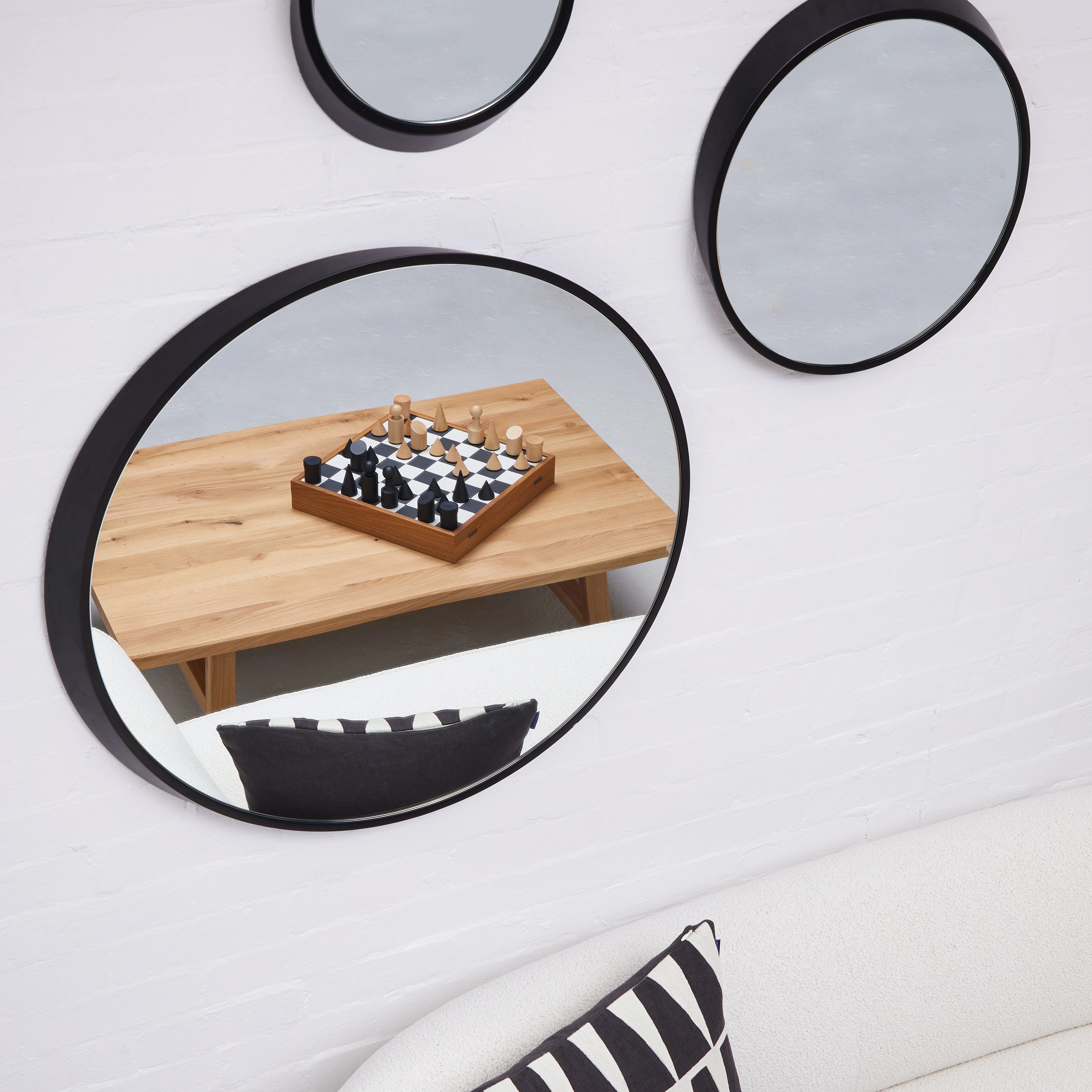 Milos Wooden Chess Set by The Conran Shop in black and white sitting on a wooden table and reflected in a round mirror