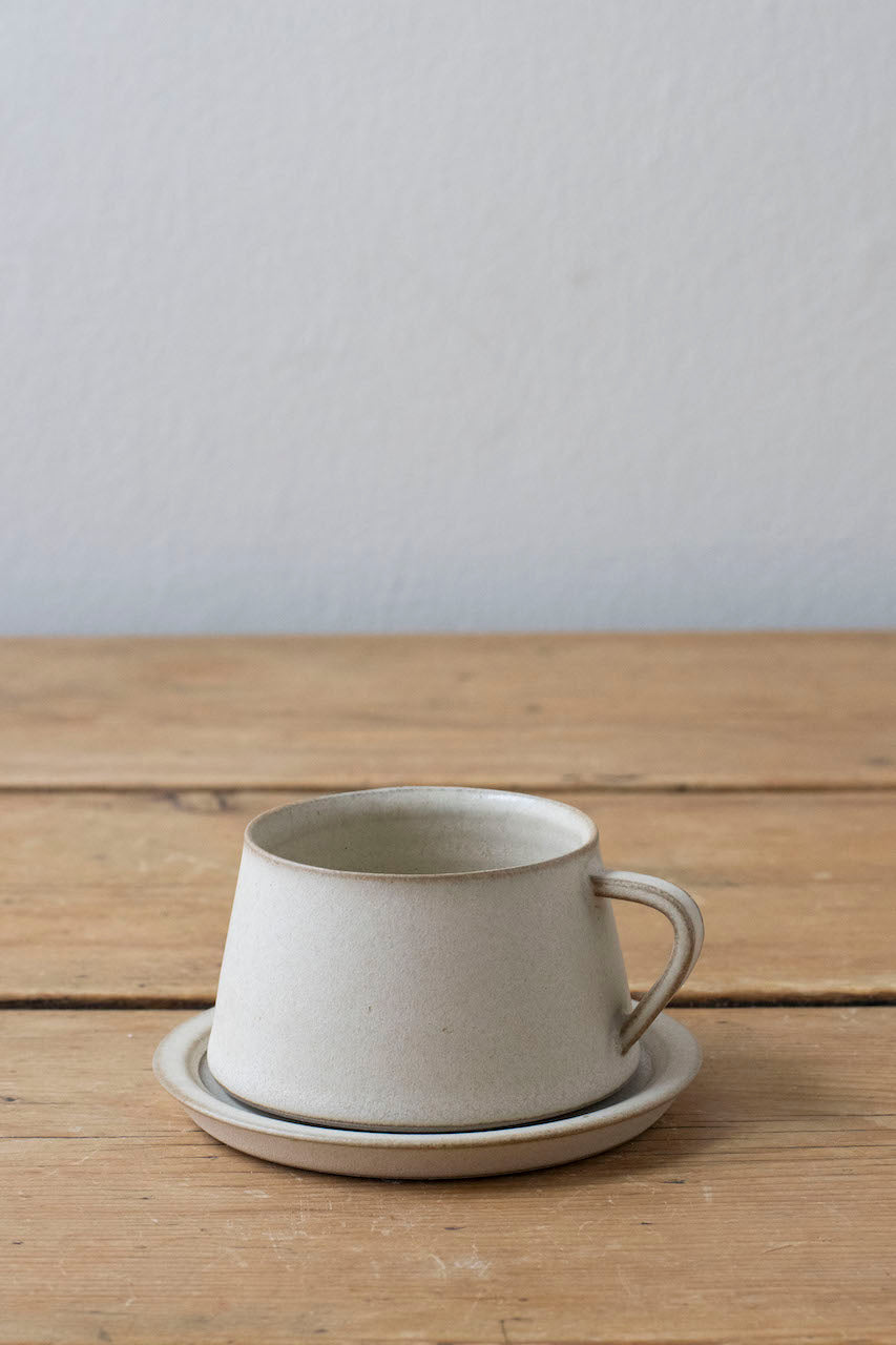 Large tapered coffee cup sitting on matching saucer in off white colourway made by Borja Moronta
