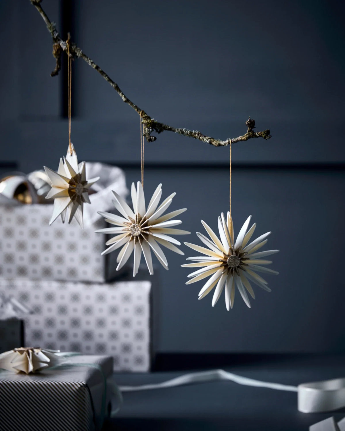 Decorative star-shaped HDStar ornaments by House Doctor, Champagne colour,  hanging from a branch against a dark background.
