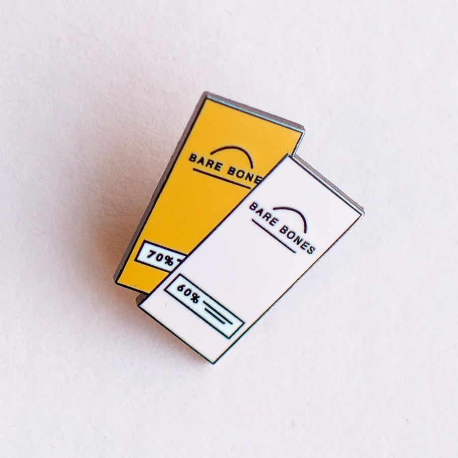 Two 'Bare Bones' chocolate bars as an enamel pin badge on a light gray background