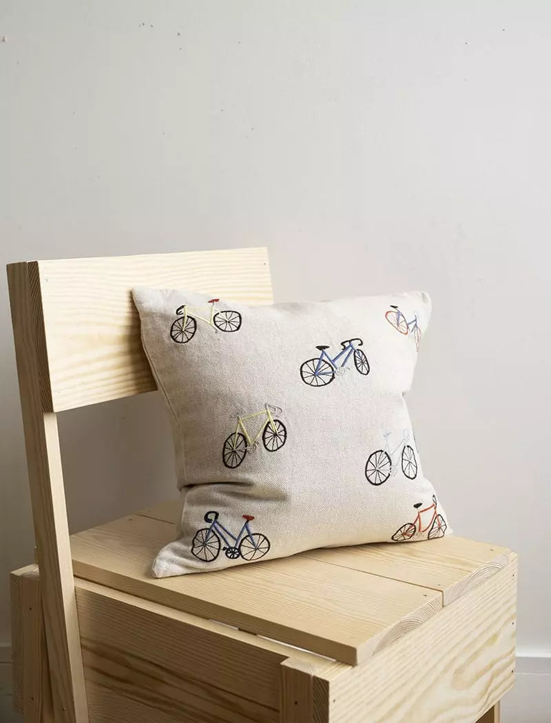 A pine chair with a square linen cushion with wobbly bicycle illustrations embroidered on the front by Fine Little Day