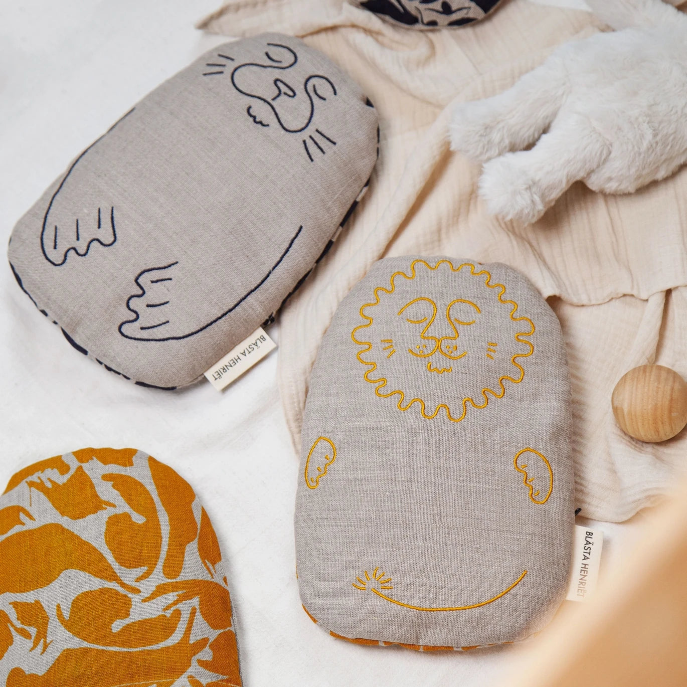 Blästa Henriët Linen Wheat & Lavender Bag Friend in seal and lion designs lying on a fabric blanket
