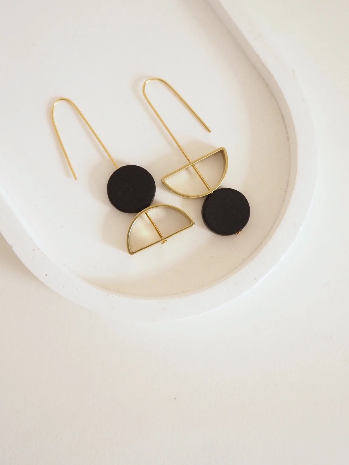A pair of Nucleo Brass and Black Upside Down Arch Earrings by brass+bold, displayed on a white ceramic dish.