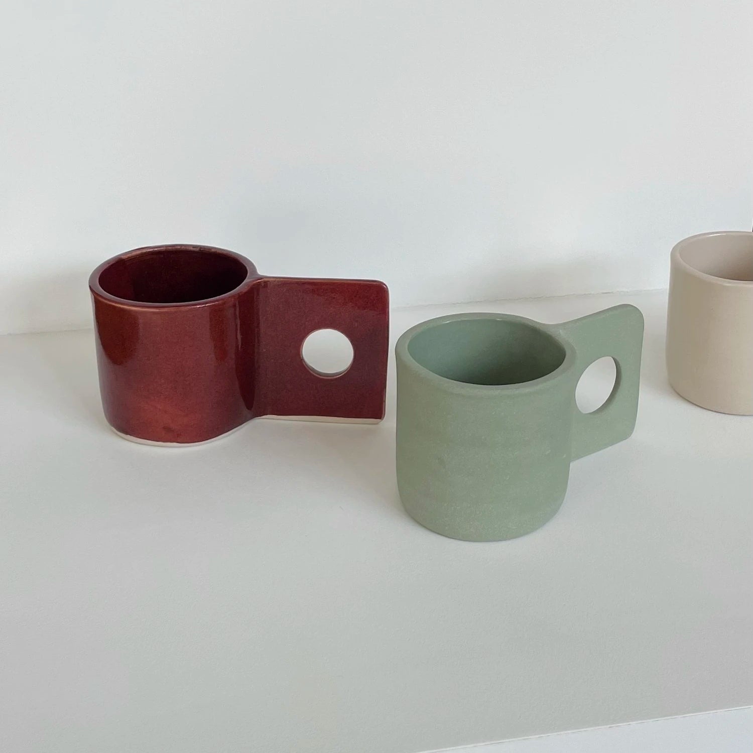 A white background with from left to right the Hopper Mug in burgundy, pistachio green and sand