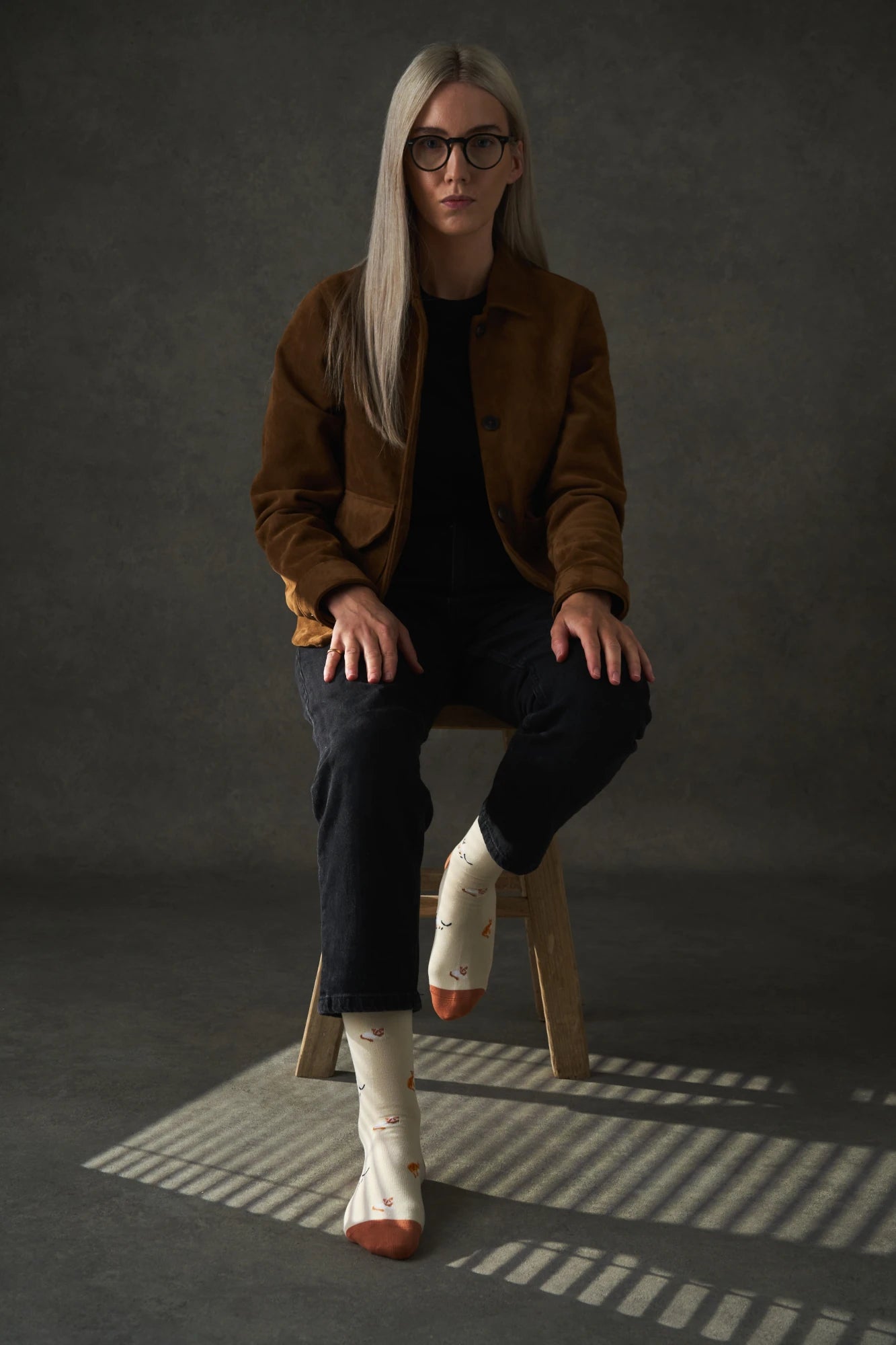 Person sitting on a stool wearing KOSI London Bamboo Cat socks against a dark background
