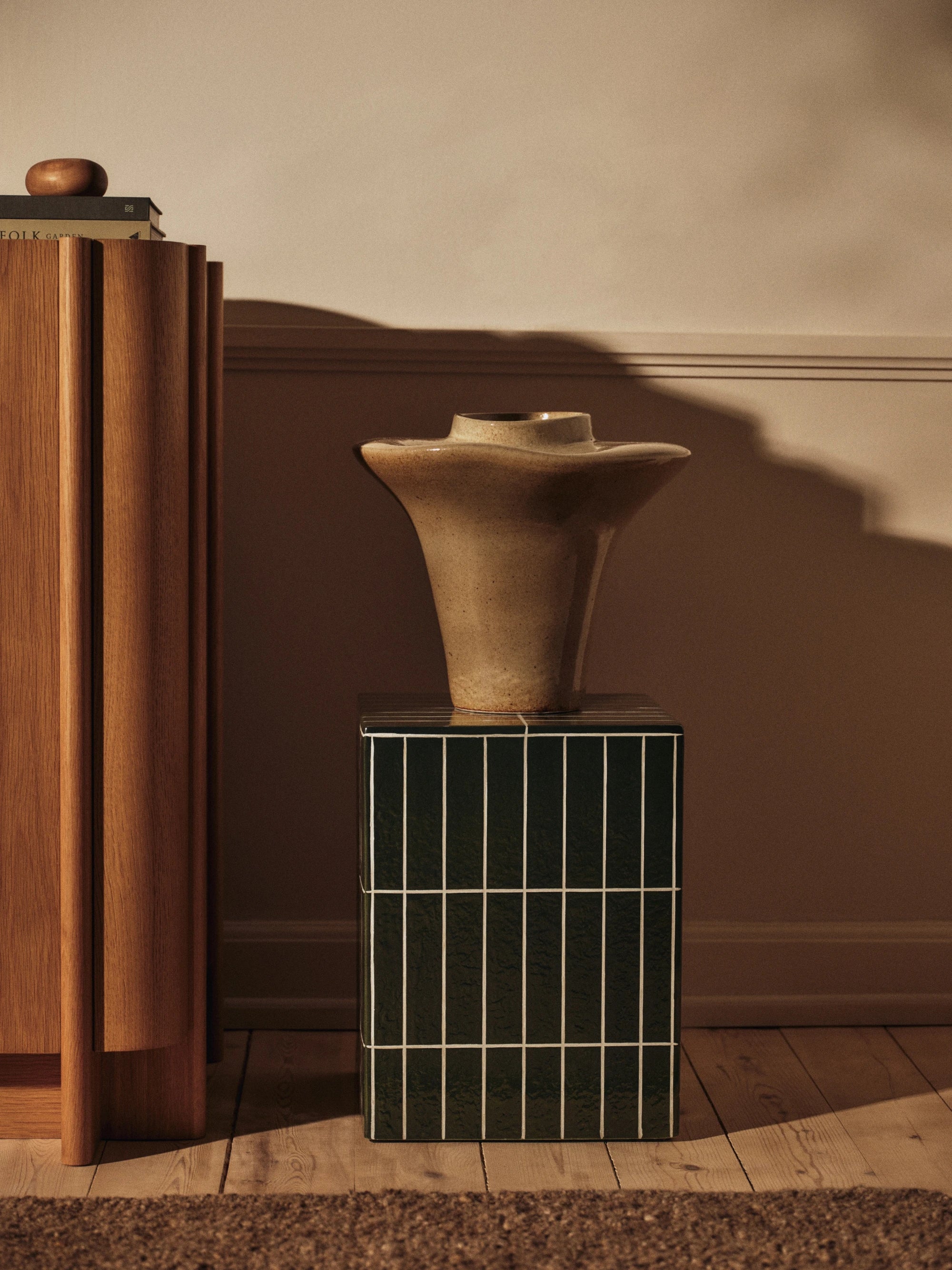 Decorative vase on a tiled pedestal against a brown wall.