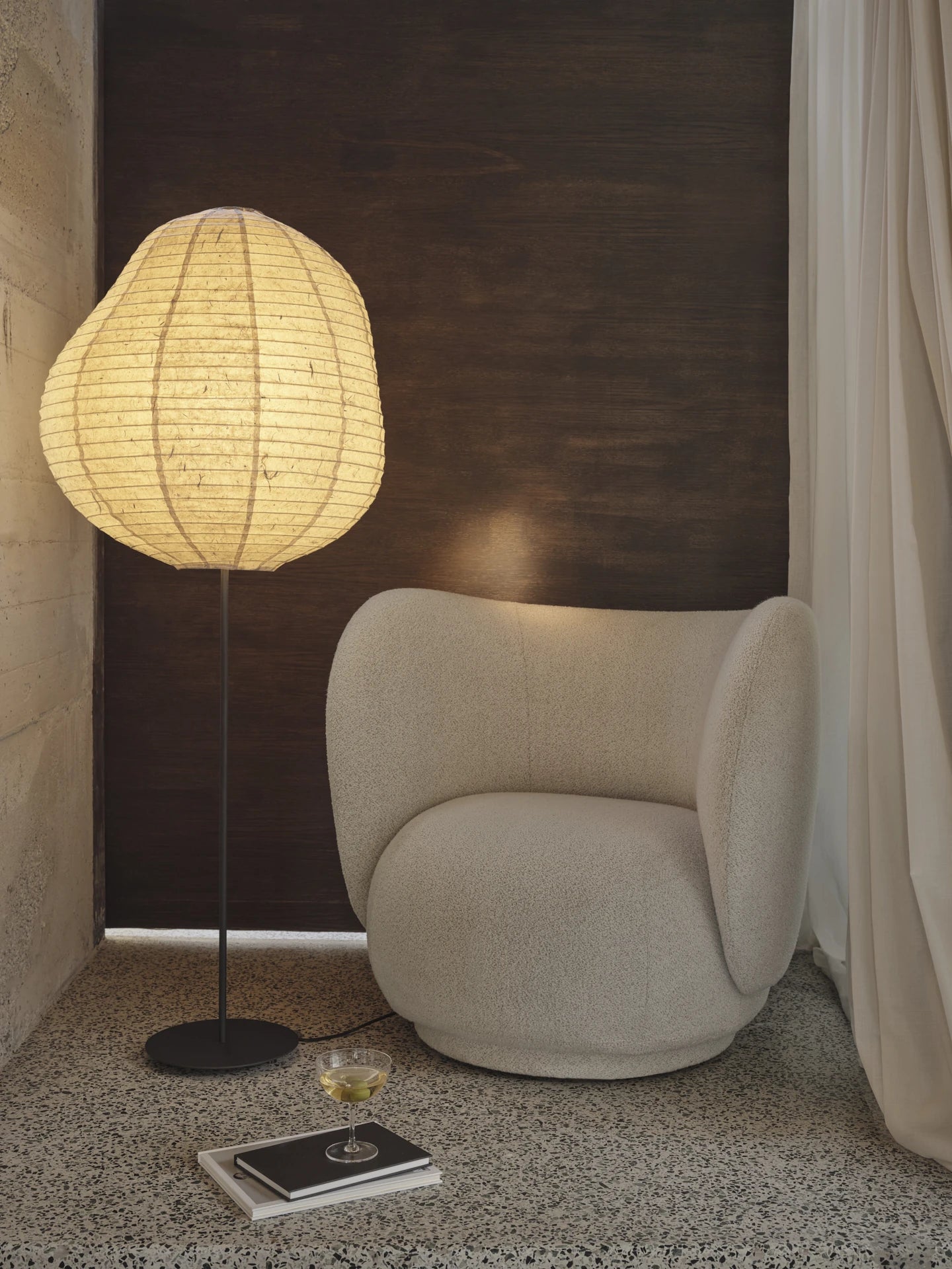 Ferm Living Rico Lounge Chair in Soft Boucle Off White in context against a dark wall and light curtain, with a tall floor standing lamp