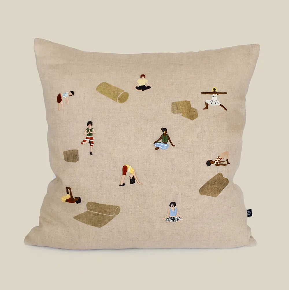 Decorative pillow with embroidered illustrations of people doing yoga poses  and yoga gear on a natural linen background