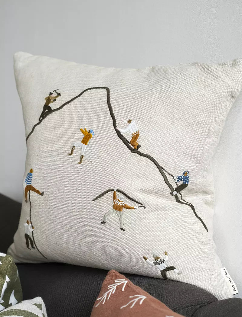 Fine Little Day 'Mountain Climbers' Embroidered Square Cushion sitting atop a dark sofa against a white wall