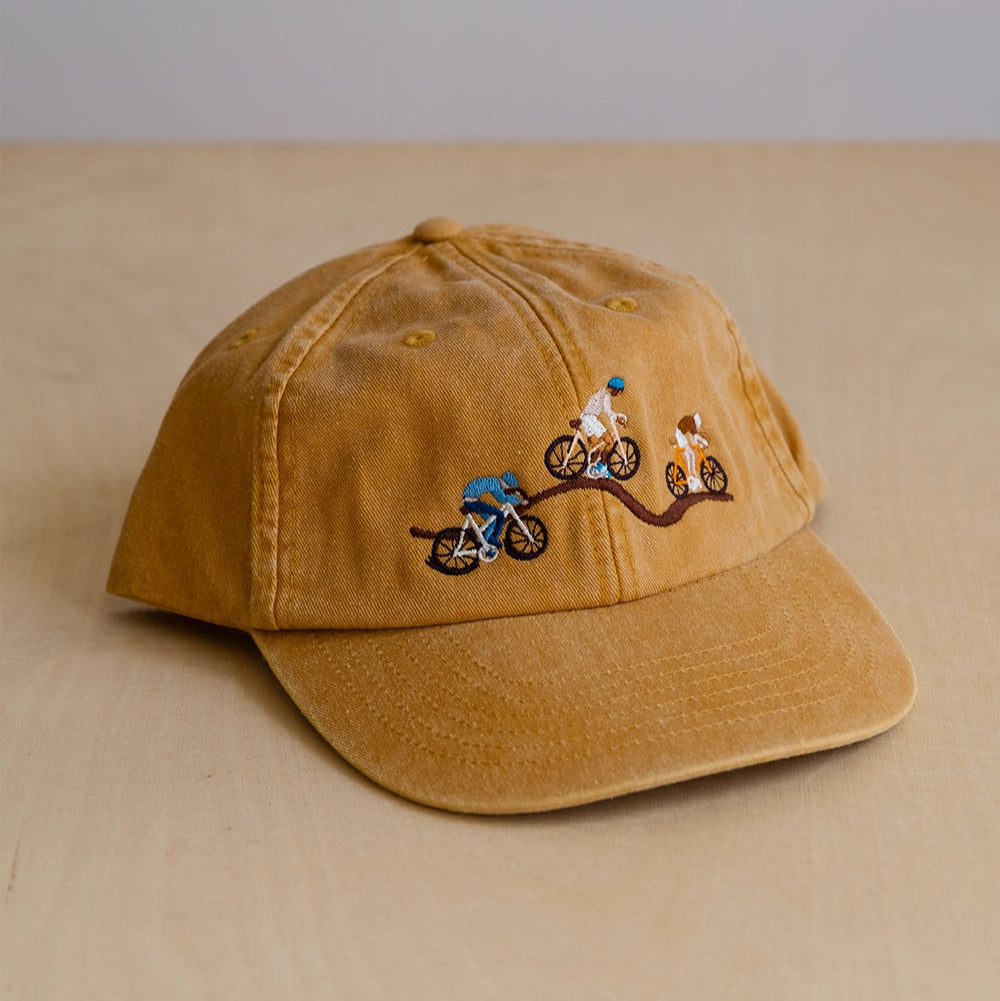 Brown ochre cap with embroidered designs of bikers on a path on a beige surface