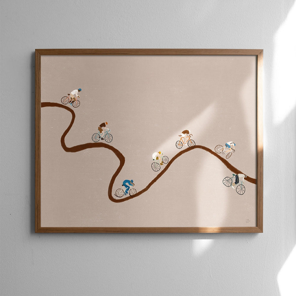 Framed artwork of cyclists on a winding road against a plain wall.