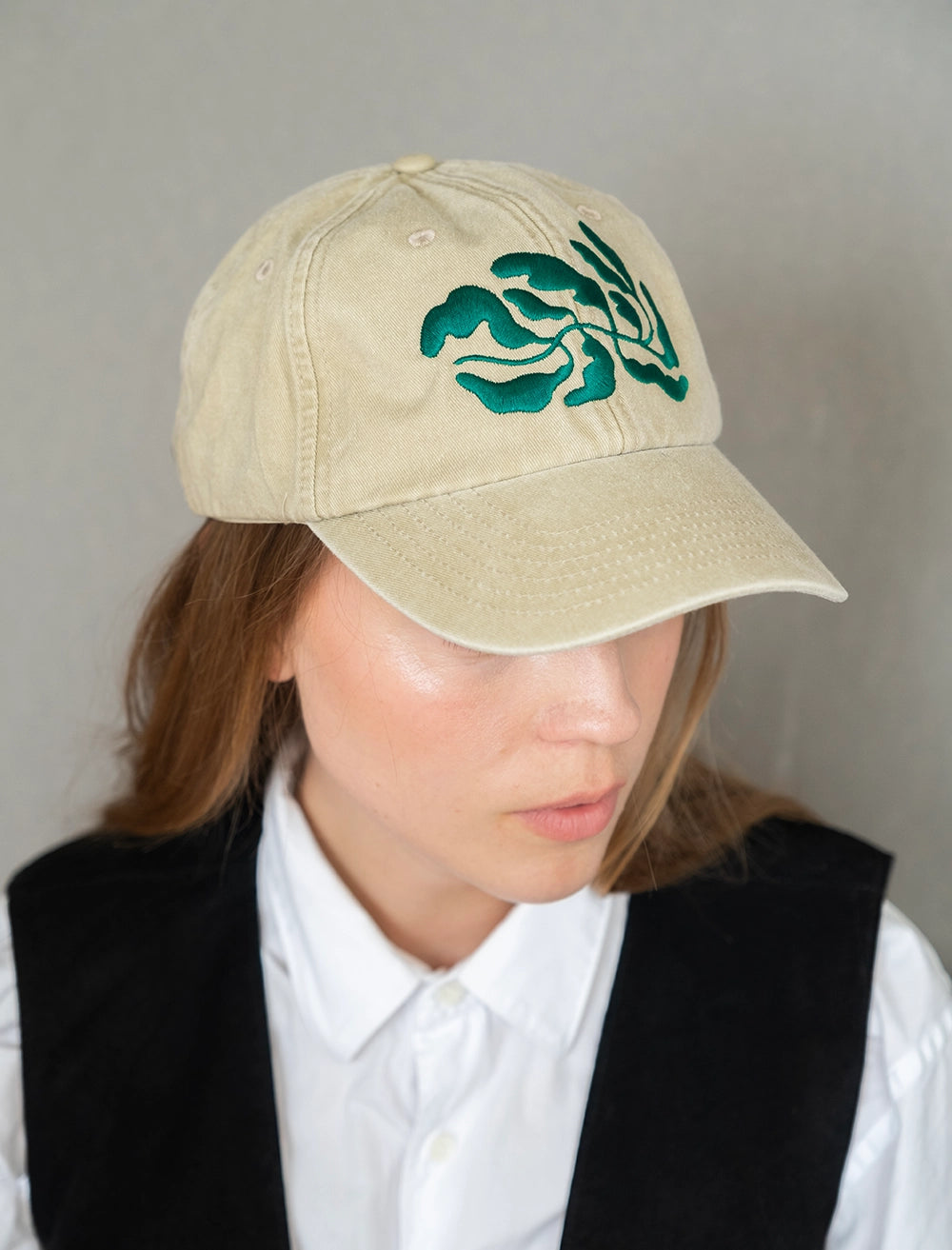 Fine Little Day Embroidered 'Leaves' 6 Panel Cap in Vintage Beige being worn by a model with long hair against a grey background