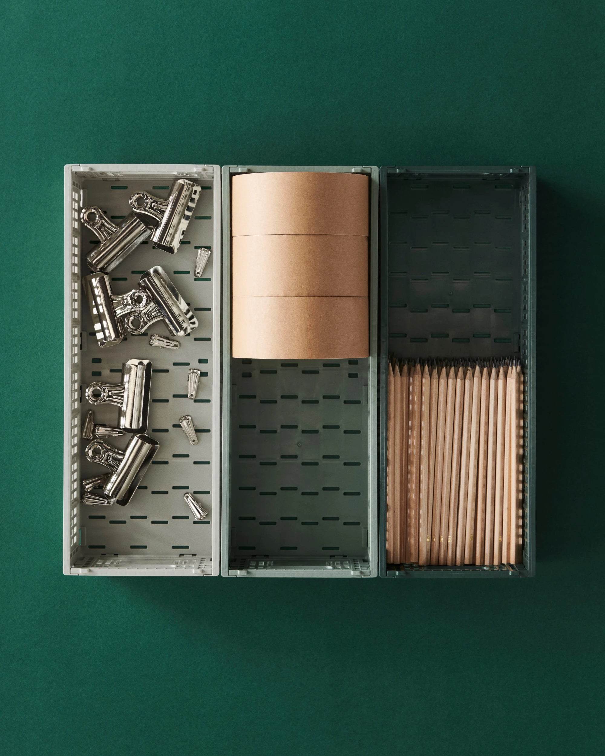HAY Colour crates with stationery items including clips, tape, and pencils on a green background | Lifestory