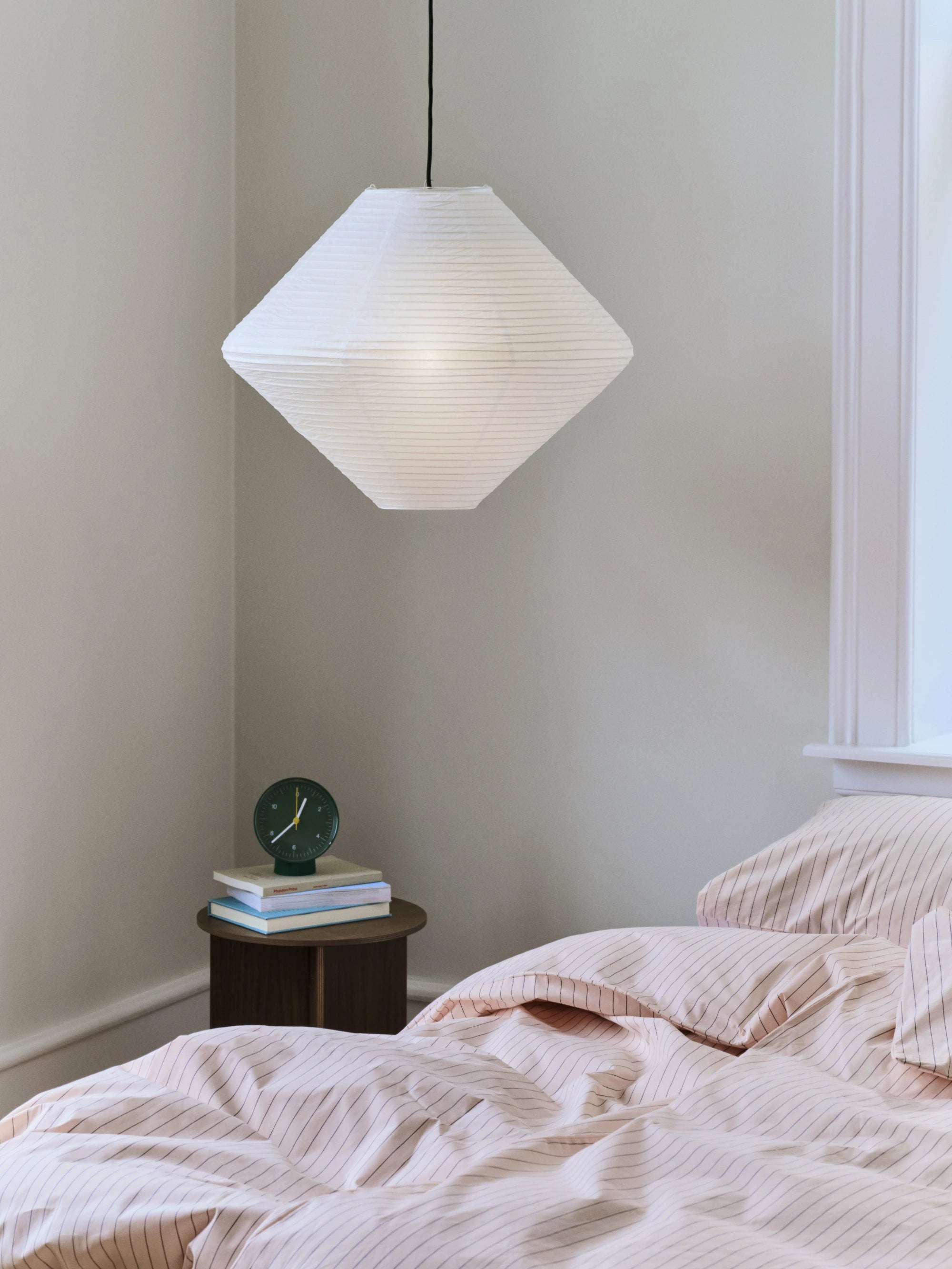 Geometric white pendant shade hanging in a bedroom setting with a bed and small table.