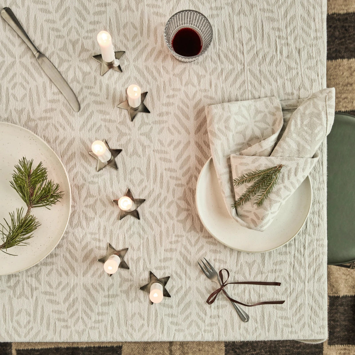 Decorative table setting with candles, plates, and napkins on a patterned tablecloth.