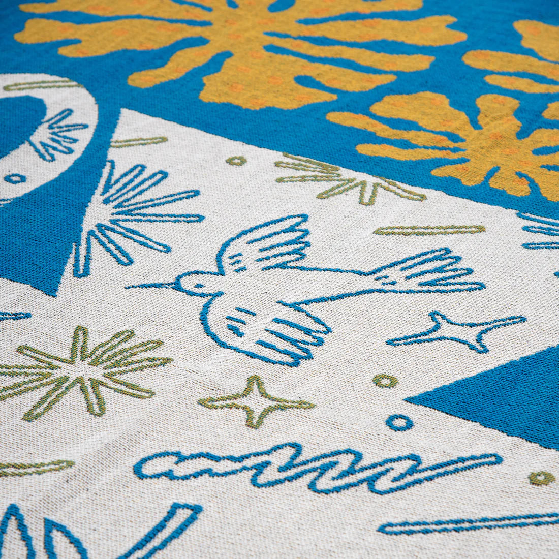 Detail of a blue, white and yellow tapestry blanket depicting a white vase and yellow flowers