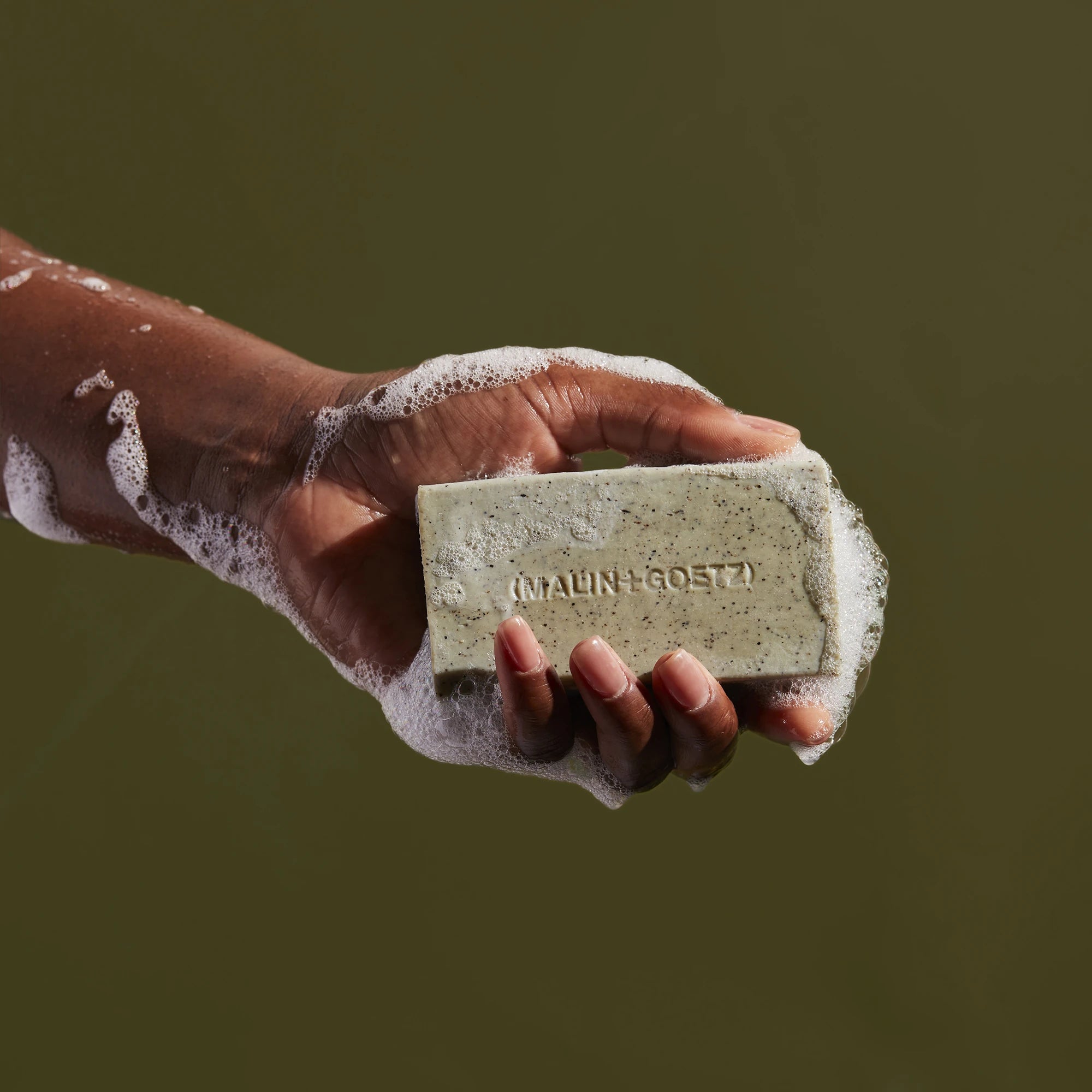 Mandelic Acid Body Exfoliating Bar by Malin+Goetz in models hand against green background