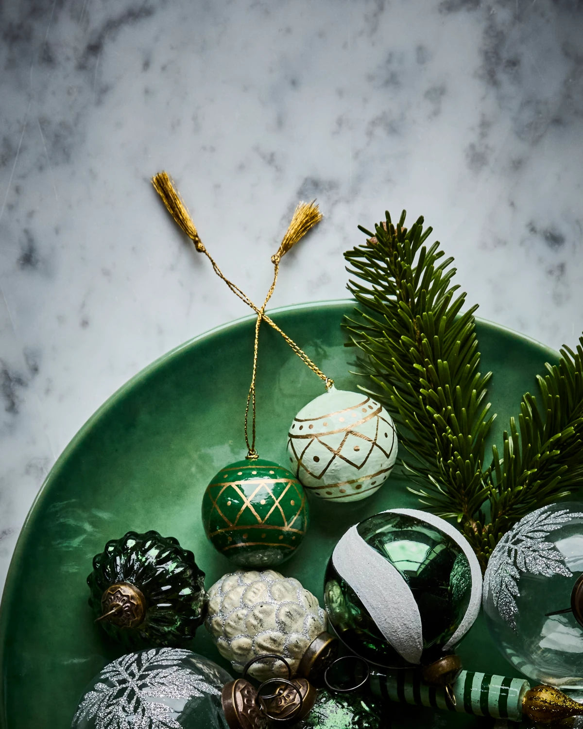 House Doctor Set of 4 'Mach' Paper Mache Hanging Ornaments lying with other ornaments on a green plate on a marble surface