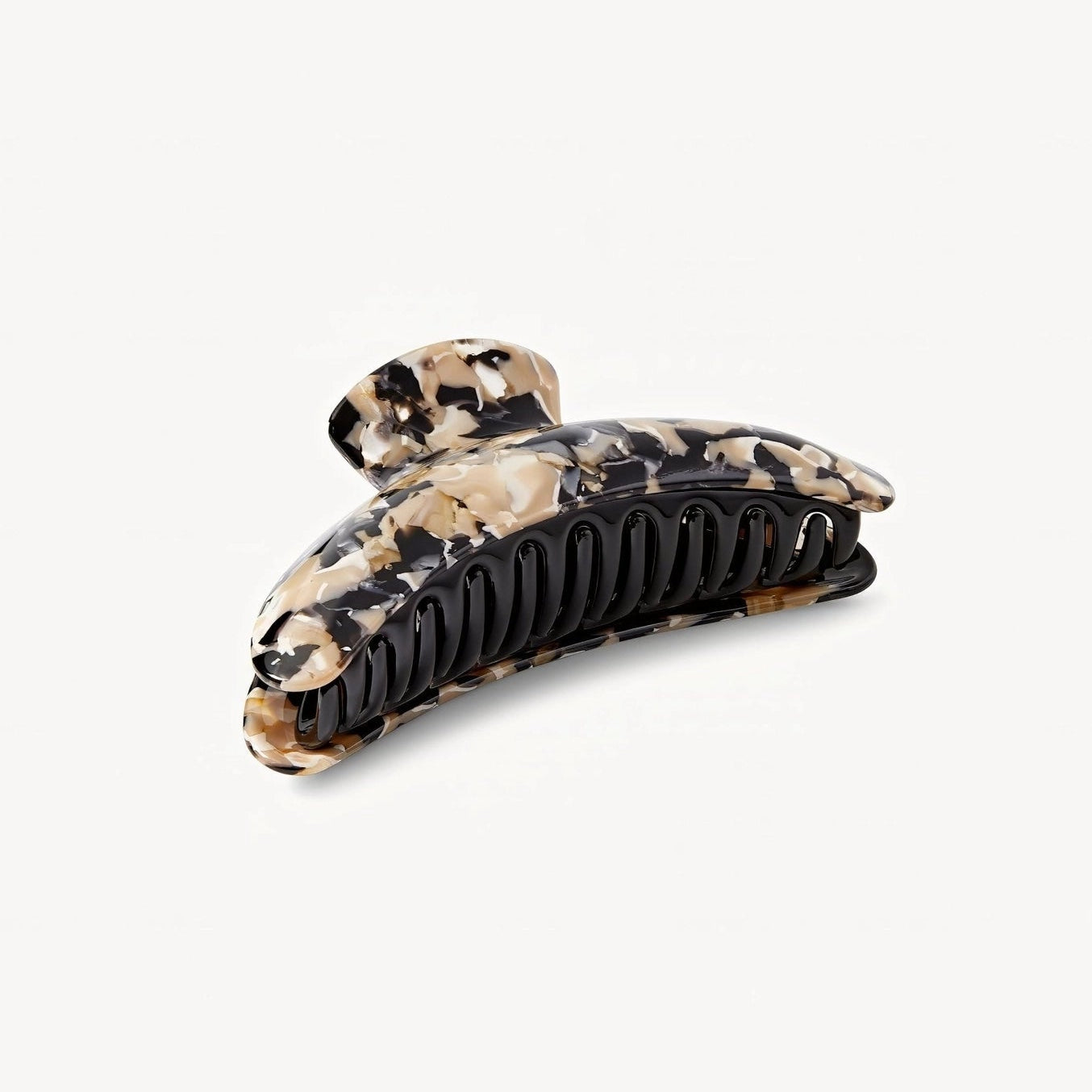 A tortoiseshell hair claw clip with a black ribbed inner jaw and a patterned outer shell in shades of beige, brown, and black, shown on a light gray background.