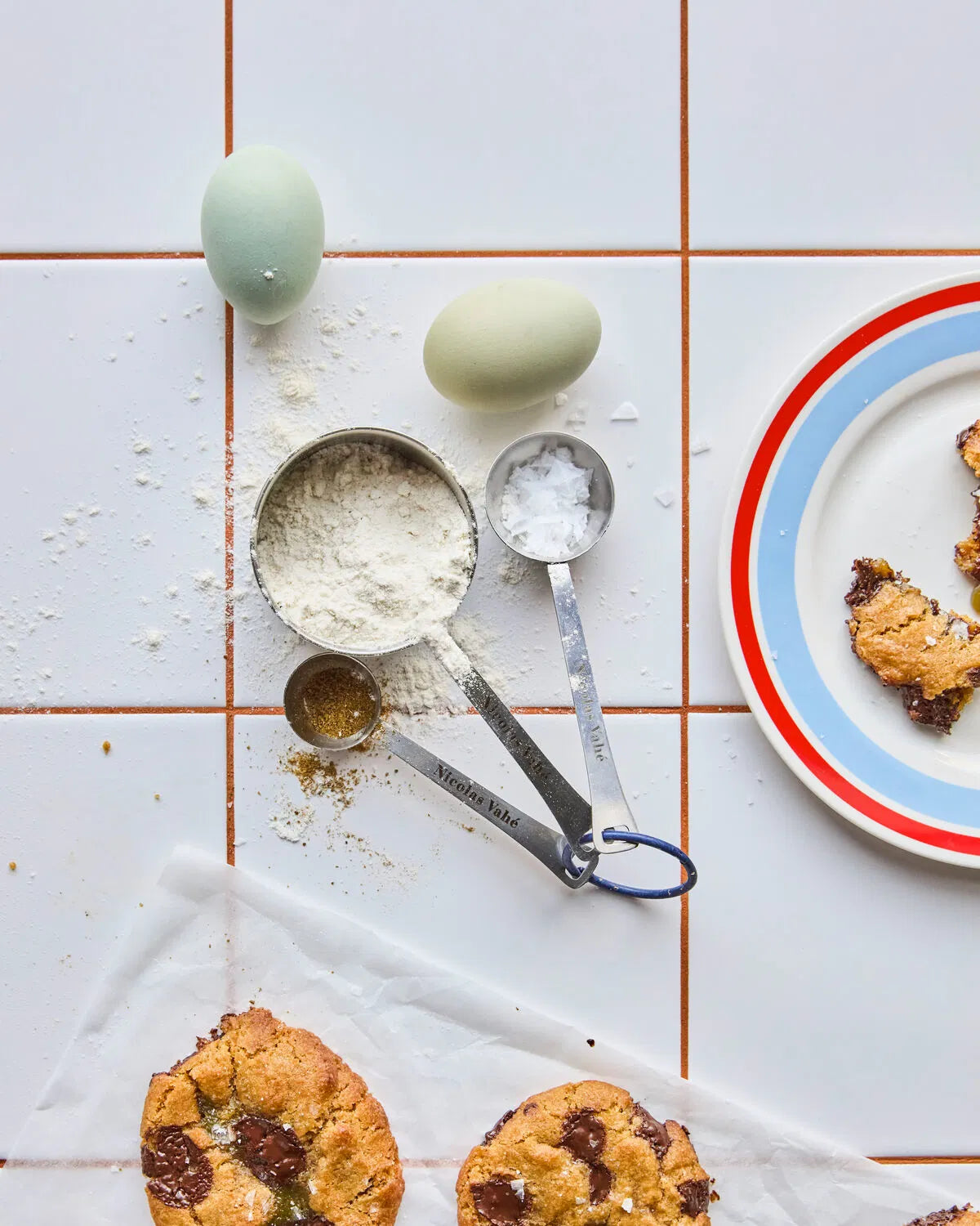 Cookies on a plate with measuring spoons and eggs on a tiled surface