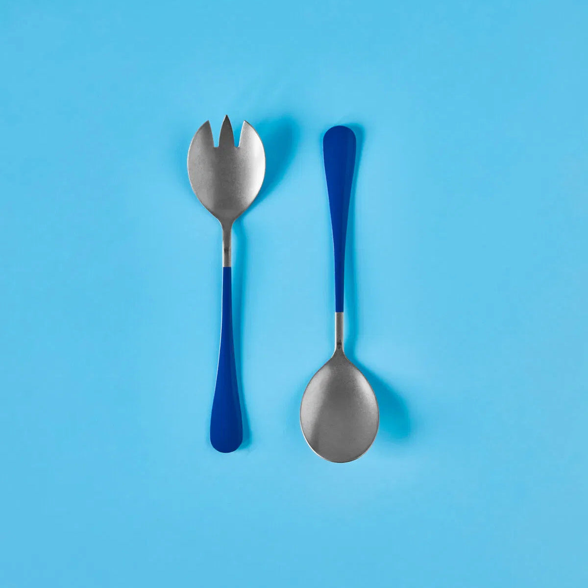 Two spoons, one with a blue handle and one with a silver handle, on a blue background.