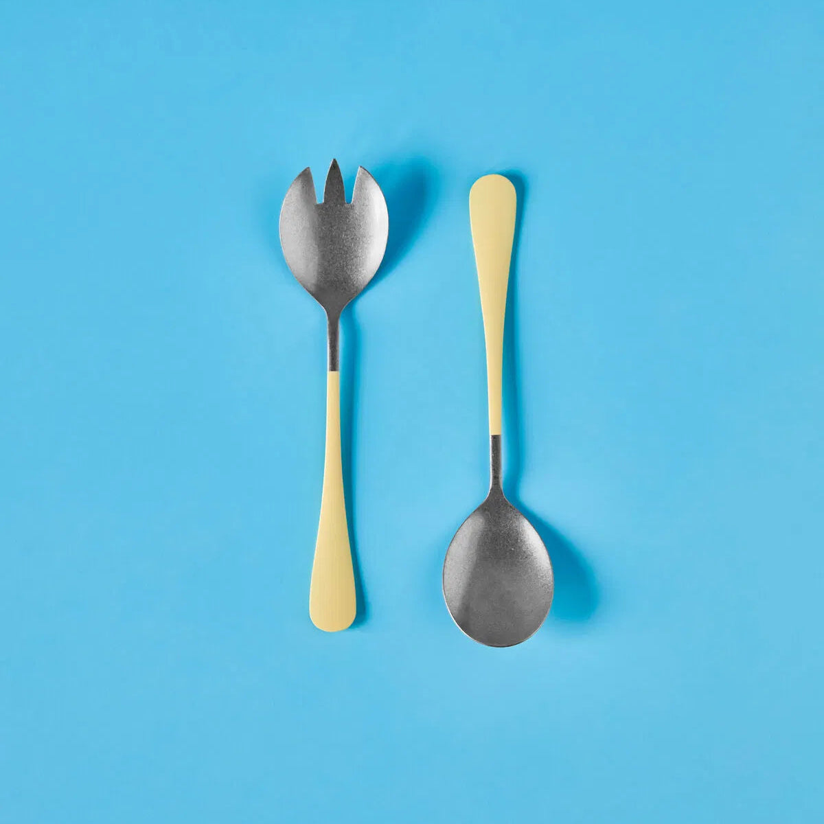 Two spoons with yellow handles on a blue background.