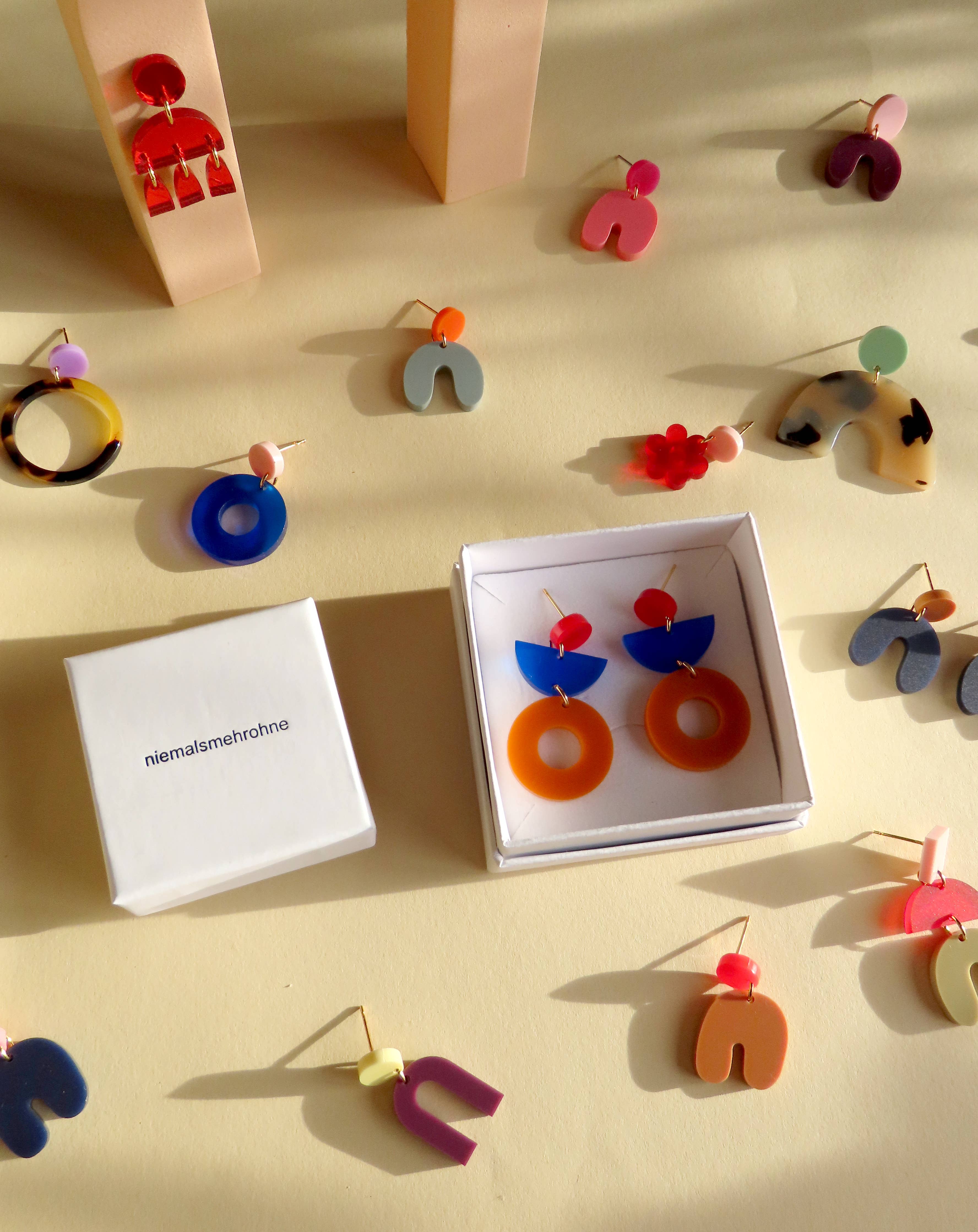 Niemalsmehrohne acrylic jewellery collection spread out on a yellow background