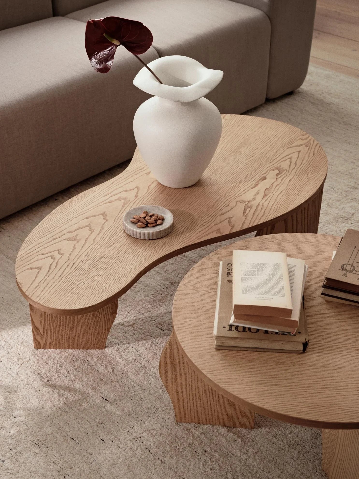 Broste Copenhagen Off-white Glazed Stoneware M Florentina Vase with a large single dark leaf, on a wooden table in front of a sofa