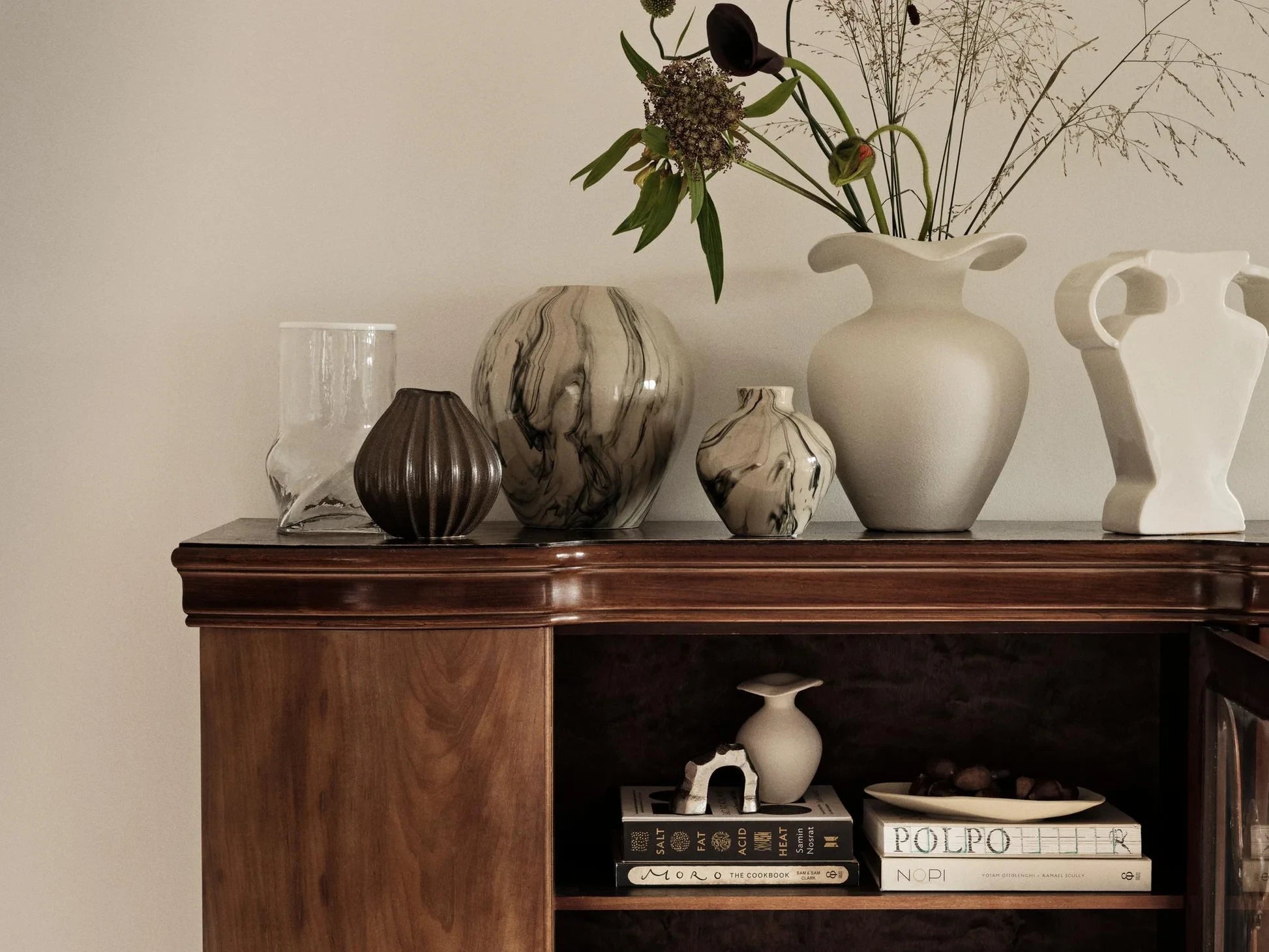 Broste Copenhagen Off-white Glazed Stoneware M Florentina Vase filled with a tall bouquet of stems on a wooden side board beside other vases