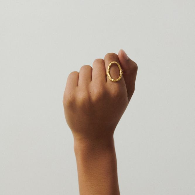 Hand wearing a gold ring on a plain background