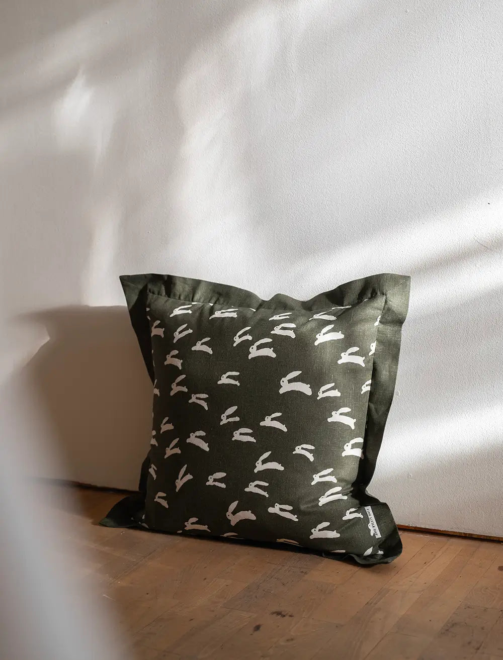 On the floor sits A square moss green cushion with playful white rabbit print by Fine Little Day