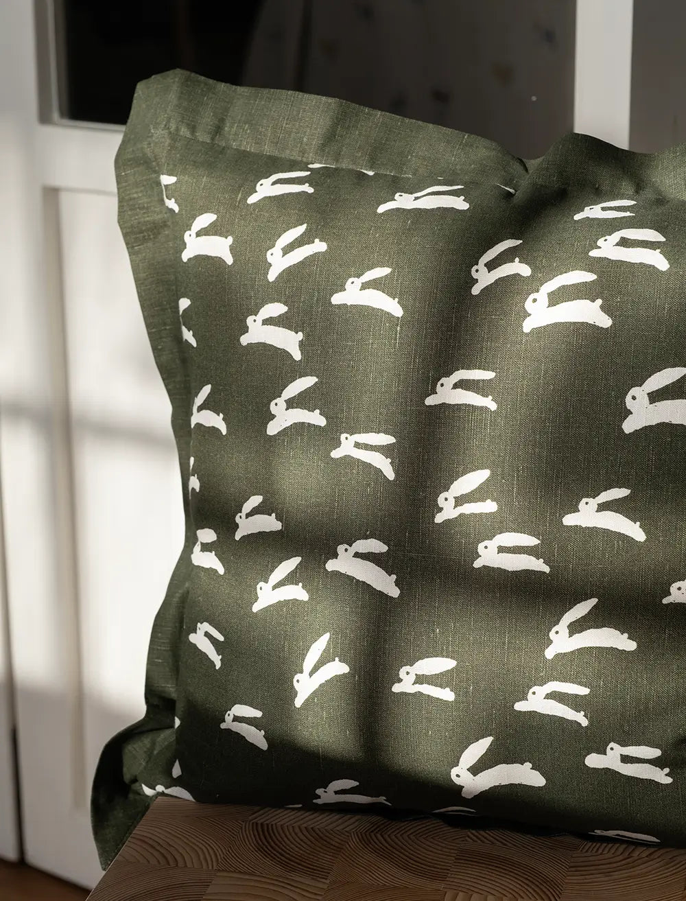 A close up of a square moss green cushion with playful white rabbit print by Fine Little Day