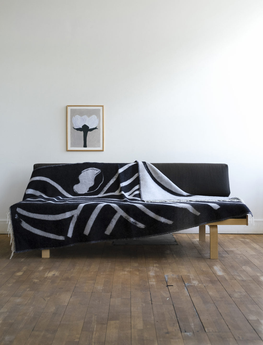 Across a sofa lies a dark grey with light grey patterned lambswool blanket from a collaboration between Sofia Lind and Fine Little Day