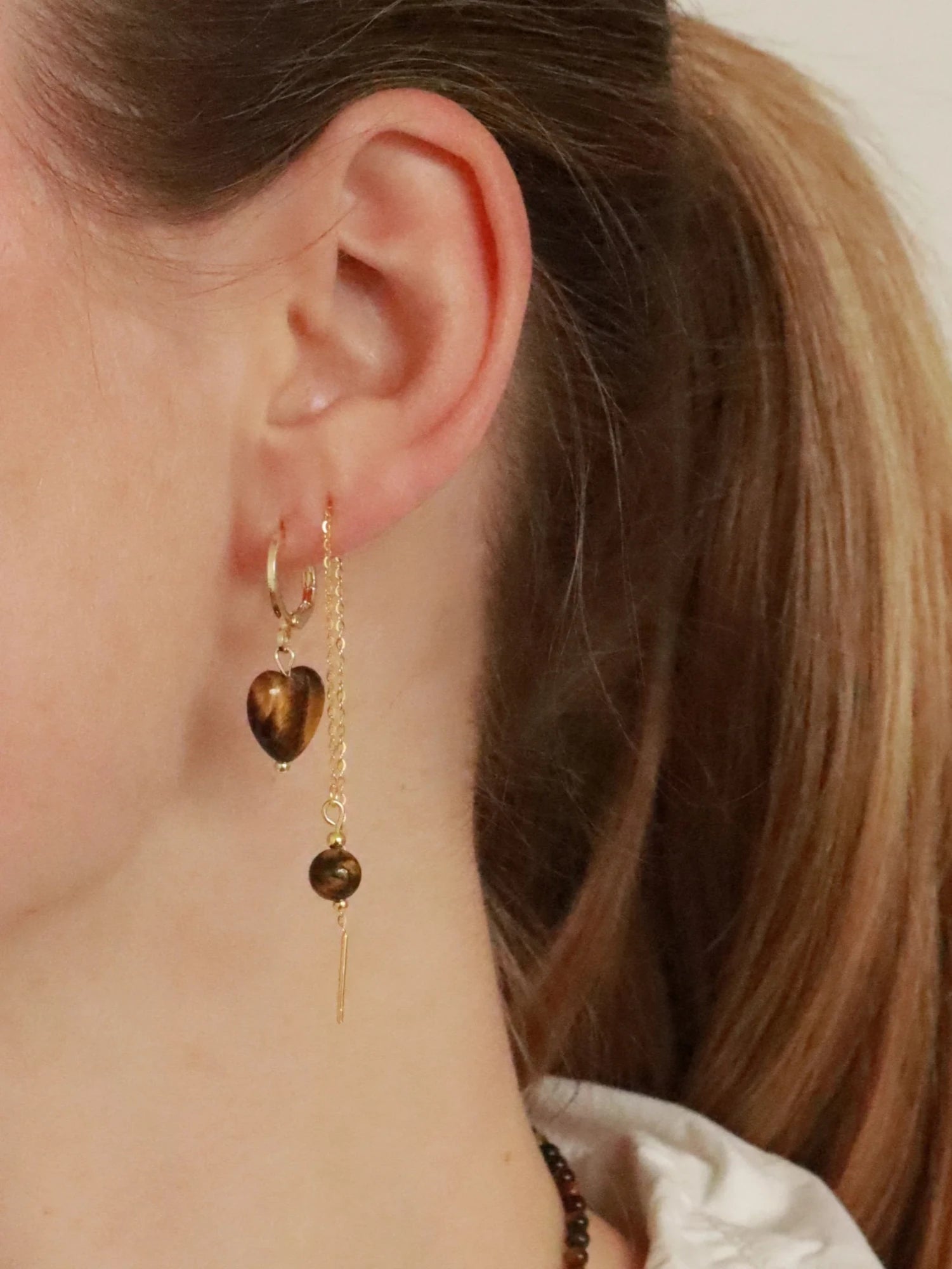 Woman wearing Soï Copenhagen Alma Tiger Eye heart earrings in 18k gold