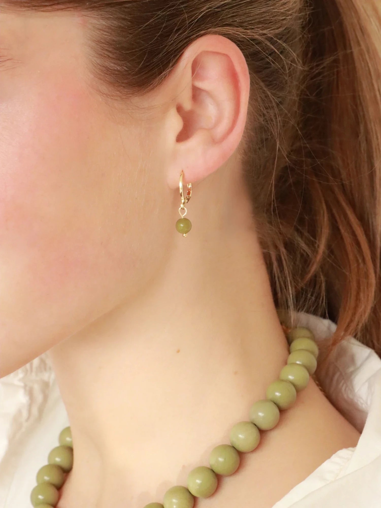 Model wearing Soï Copenhagen Ava huggie hoop earrings in 18k gold with a Green Alashan Agate stone