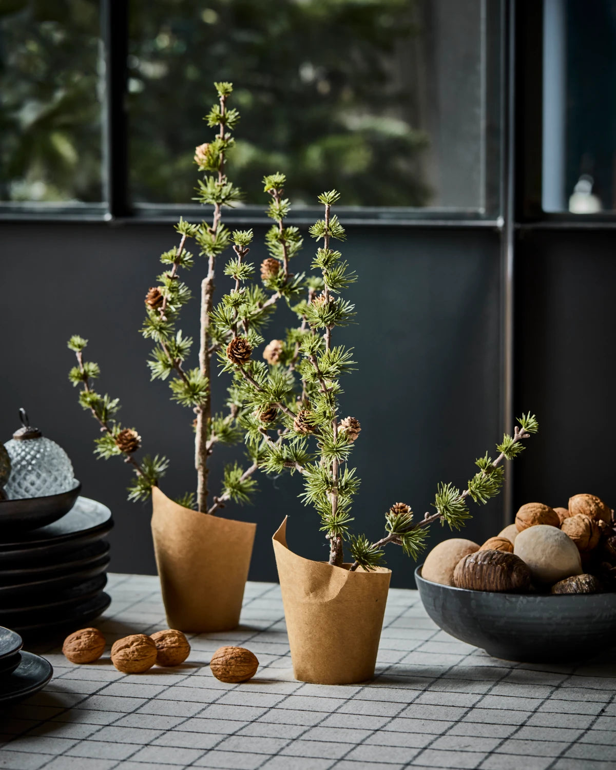 House Doctor 'Stay' Christmas Cedar Tree - 40cm wrapped in brown paper pots sitting on a tablecloth amidst a bowl of nuts and tableware