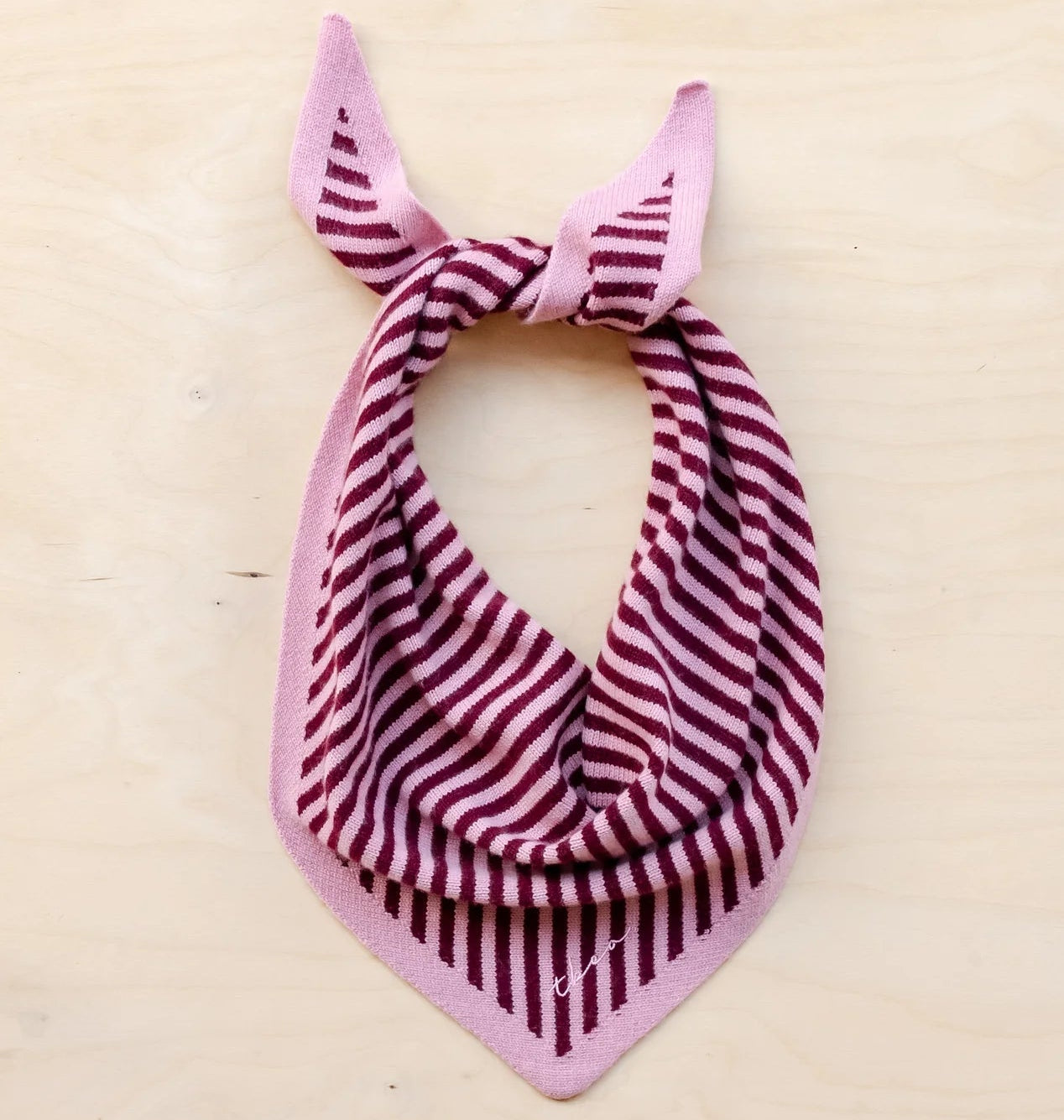 Pink and burgundy striped merino wool scarf with a knot on a beige background
