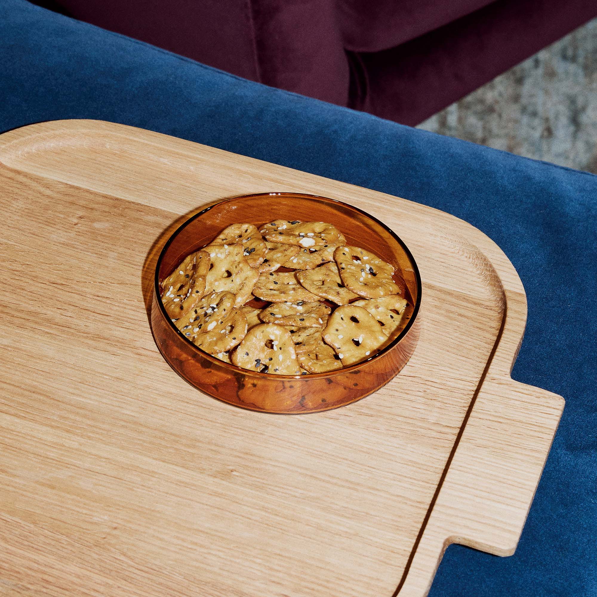 Amber glass bowl with crackers on a wooden tray against a blue fabric background