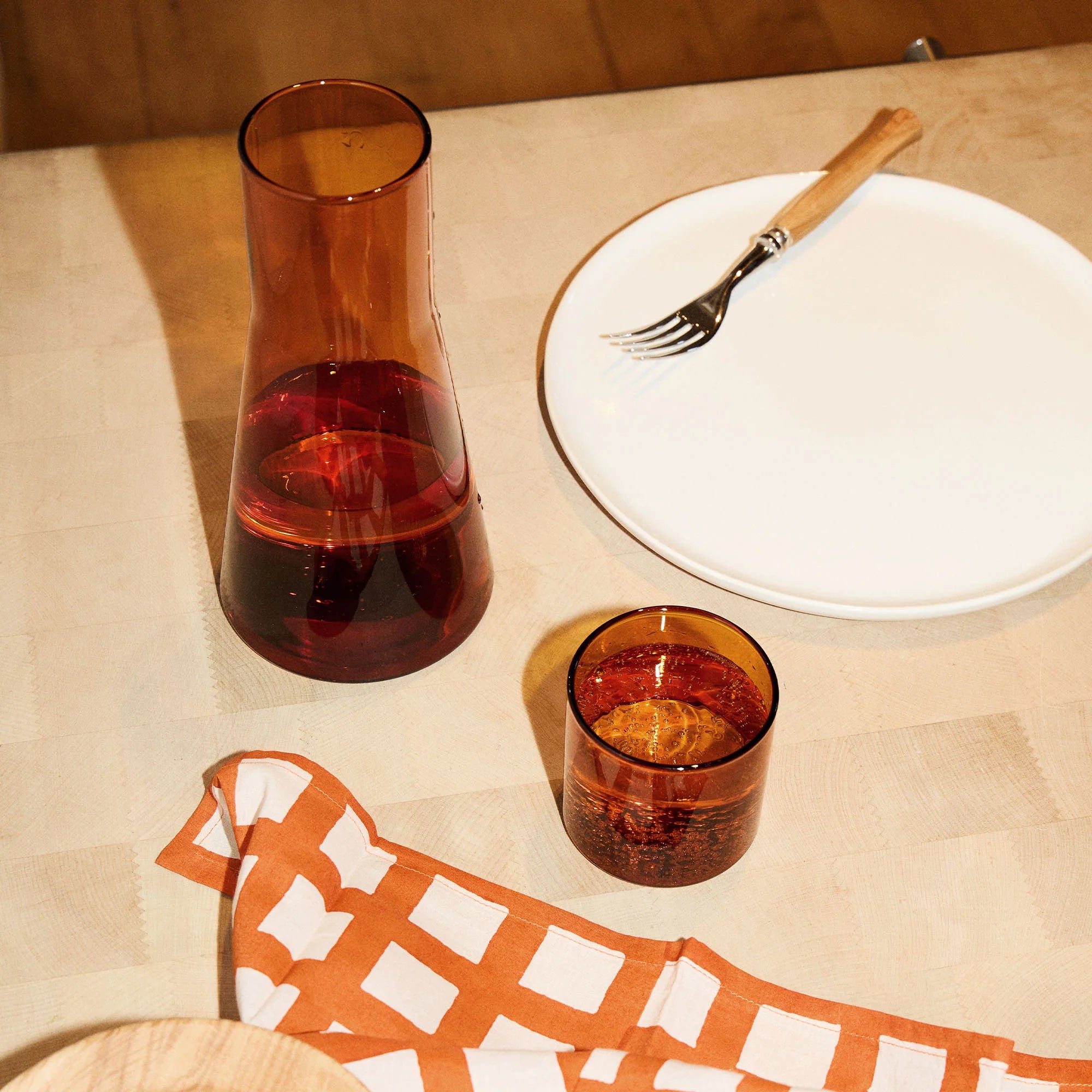 Amber glass carafe and glass on a table with a white plate and fork.