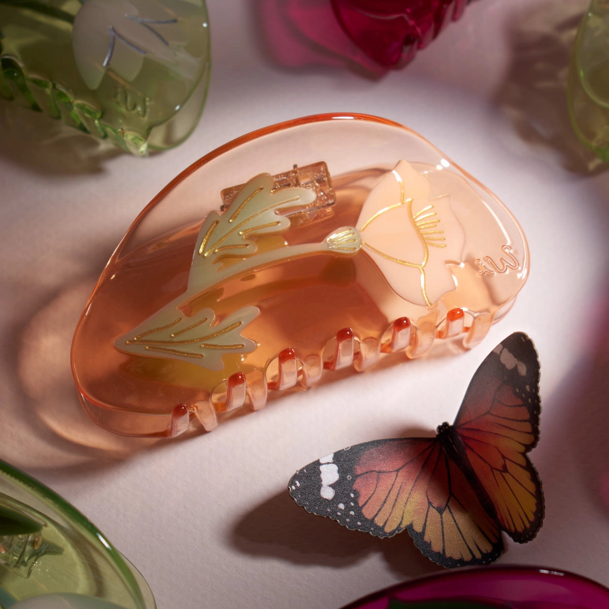 Winona Irene California Poppy Wildflower Acetate Hair Claw on a white surface next to a paper butterfly