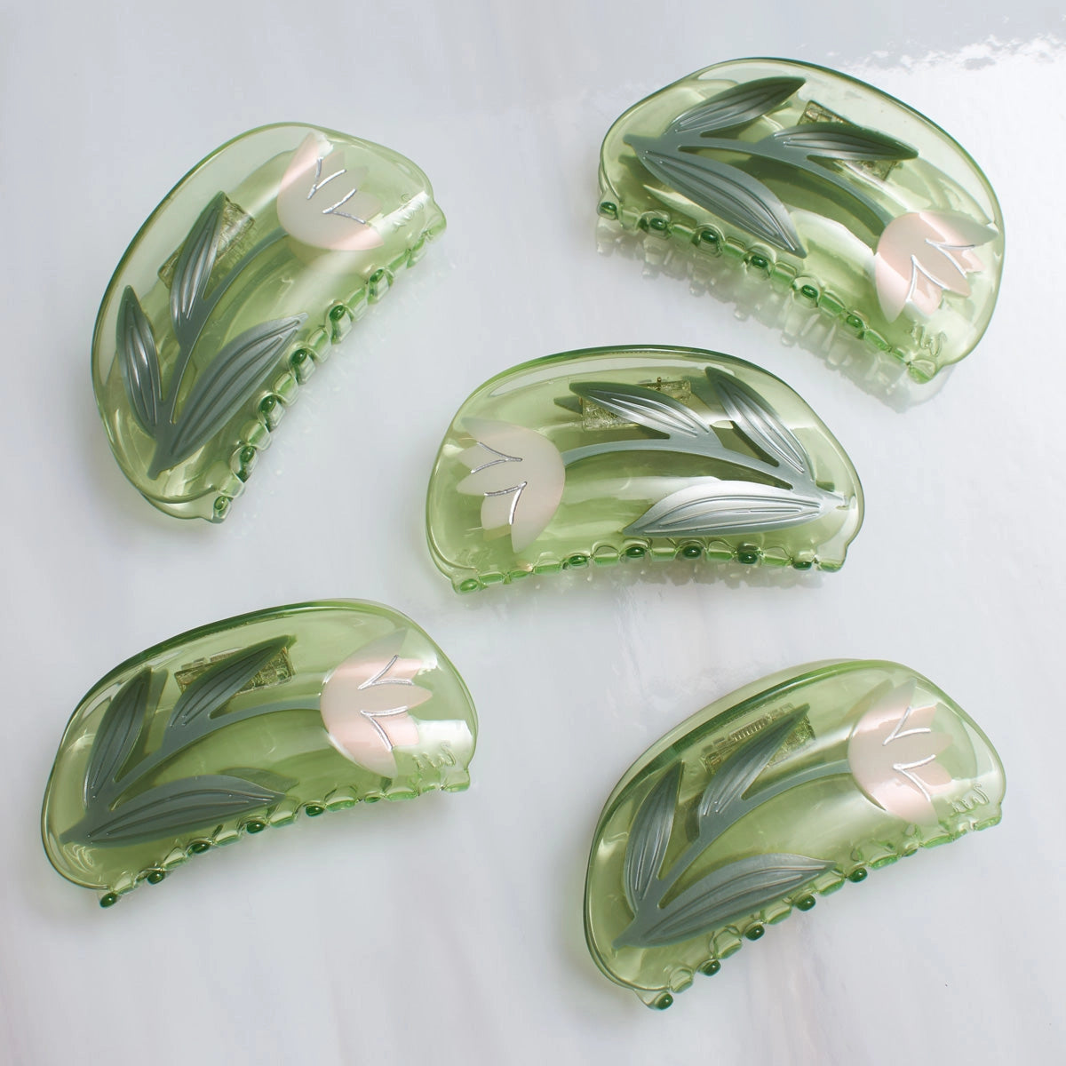 Five green hair clips with floral designs on a white background
