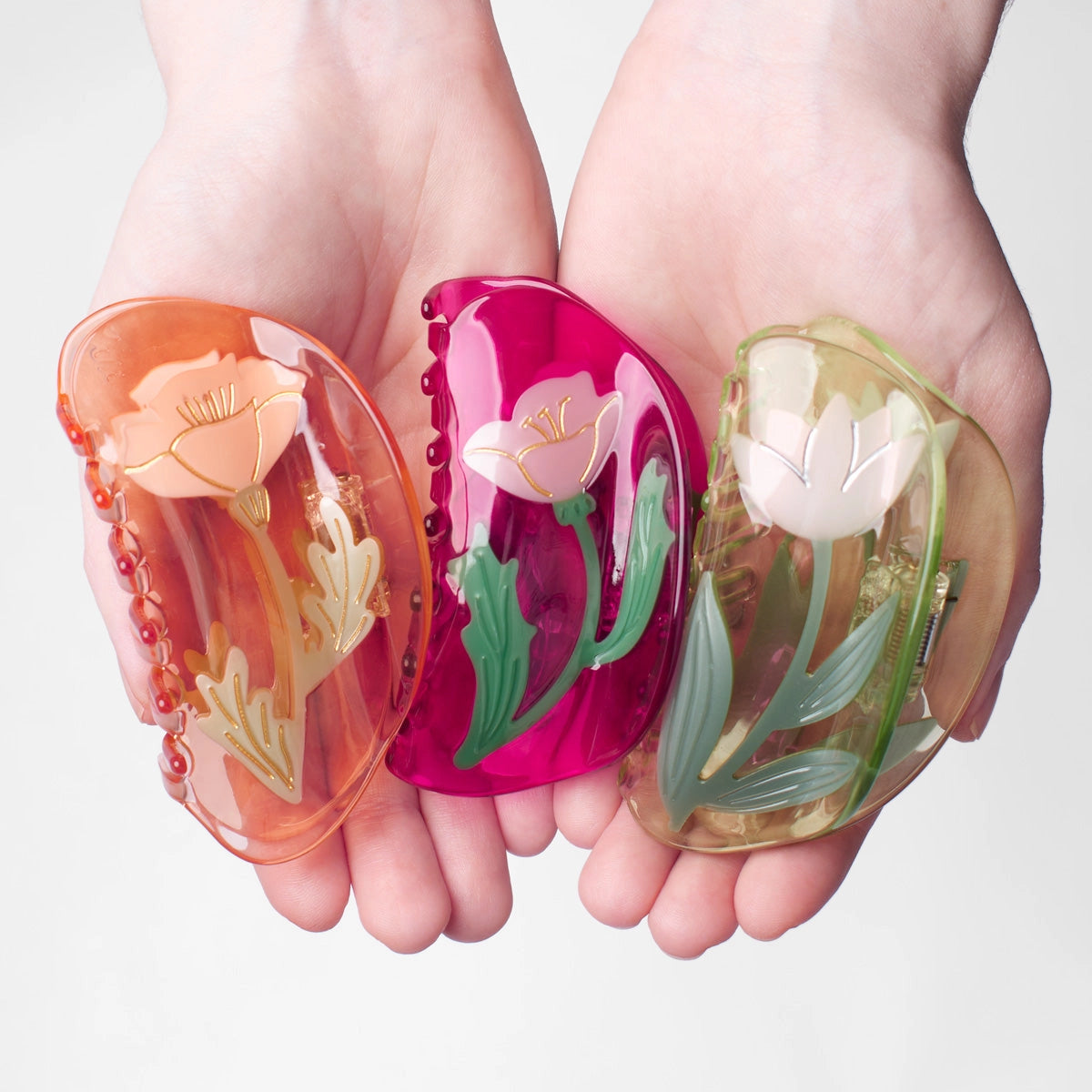 Three floral hair claw designs held by a person's hands.