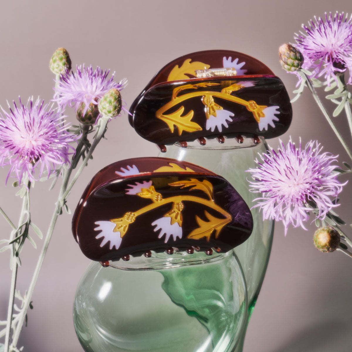 Winona Irene Milk Thistle Acetate Hair Claws balanced on green glass jars and surrounded by thistles