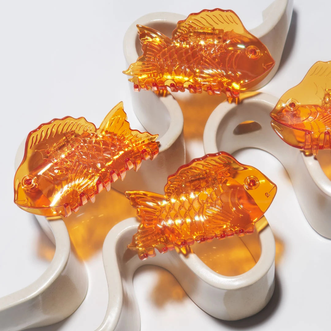 A group of Winona Irene Sea Bream Ocean Fish Acetate Hair Claws  in clear orange on a white wavey ceramic dish
