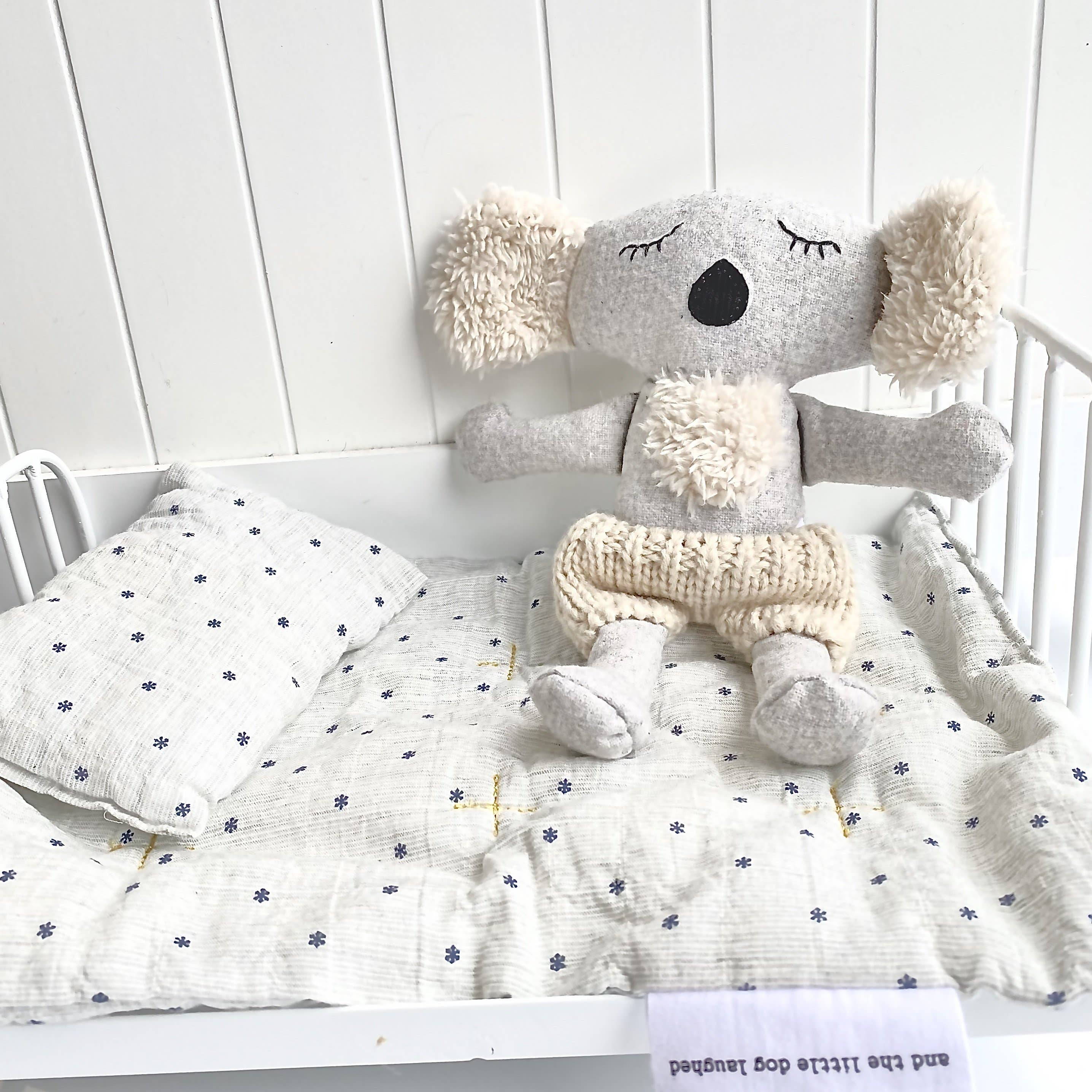 Plush grey toy koala sitting against a wall in a light grey crib